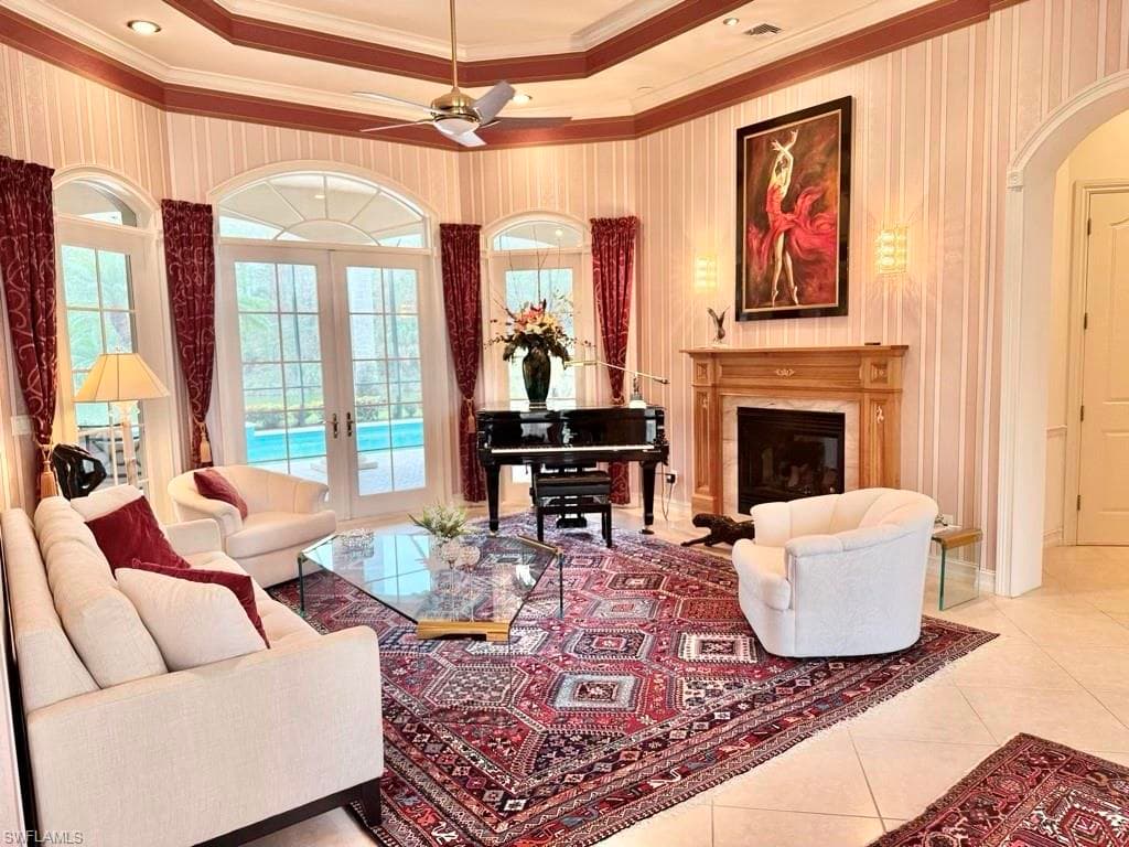 Living room with light tile patterned floors, crown molding, a high end fireplace, french doors, and a raised ceiling