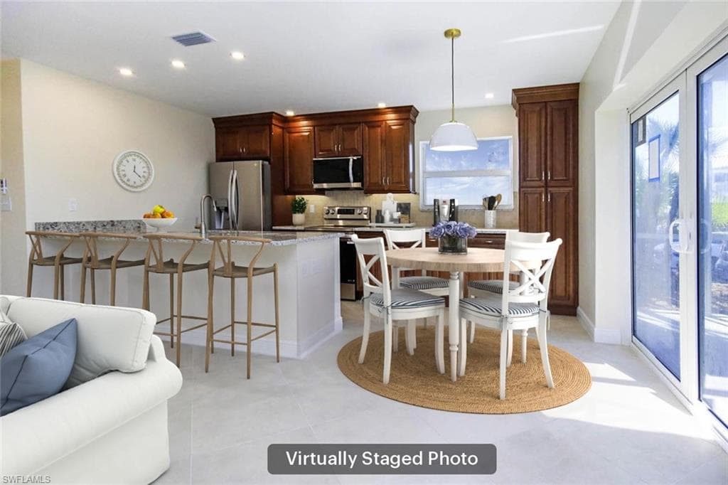 Kitchen with a breakfast bar area, pendant lighting, stainless steel appliances, light stone countertops, and backsplash