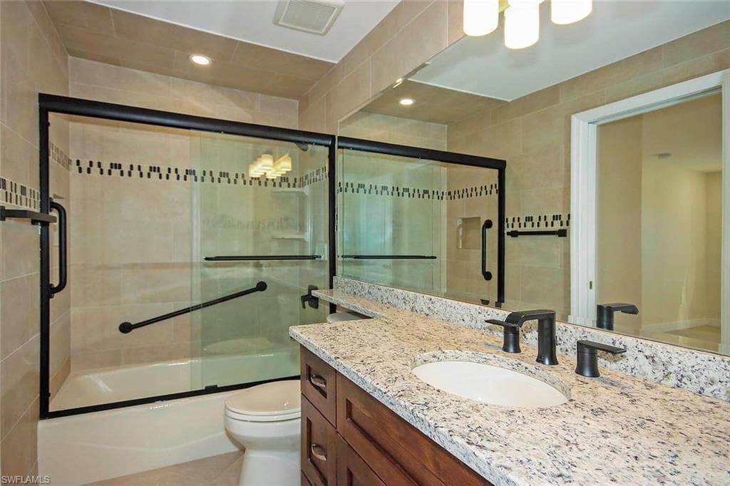Full bathroom with enclosed tub / shower combo, vanity, tile patterned floors, and toilet