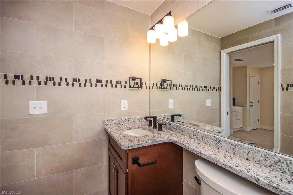 Bathroom featuring vanity, toilet, and tile walls