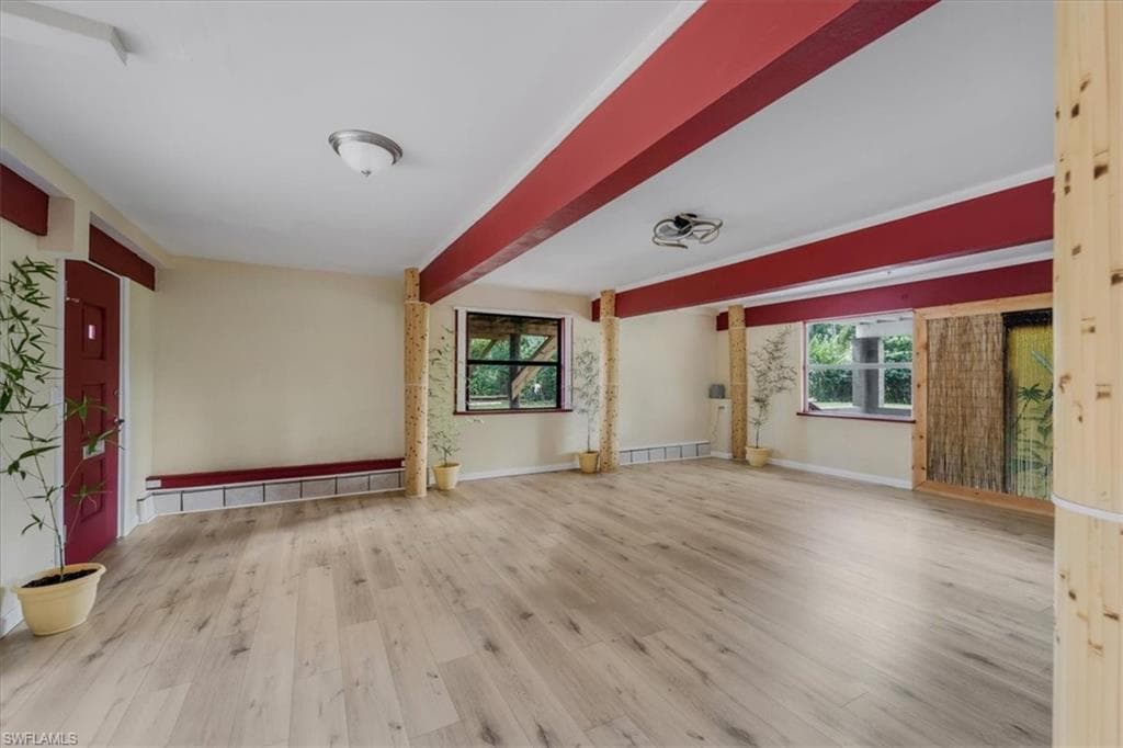 Unfurnished living room featuring beam ceiling and light hardwood / wood-style flooring