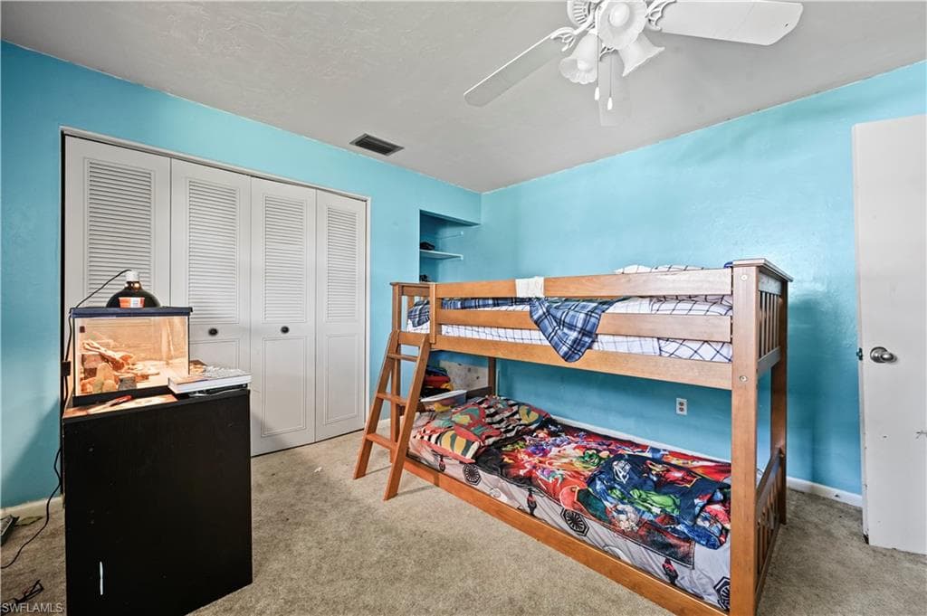 Carpeted bedroom with ceiling fan and a closet