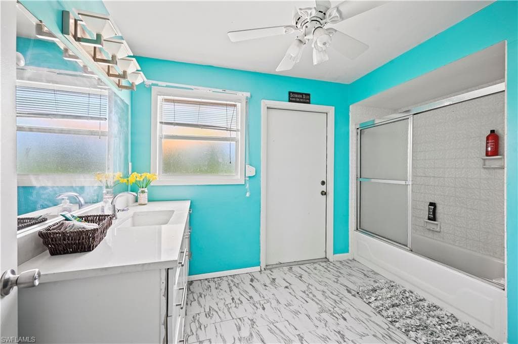 Bathroom with bath / shower combo with glass door, vanity, and ceiling fan