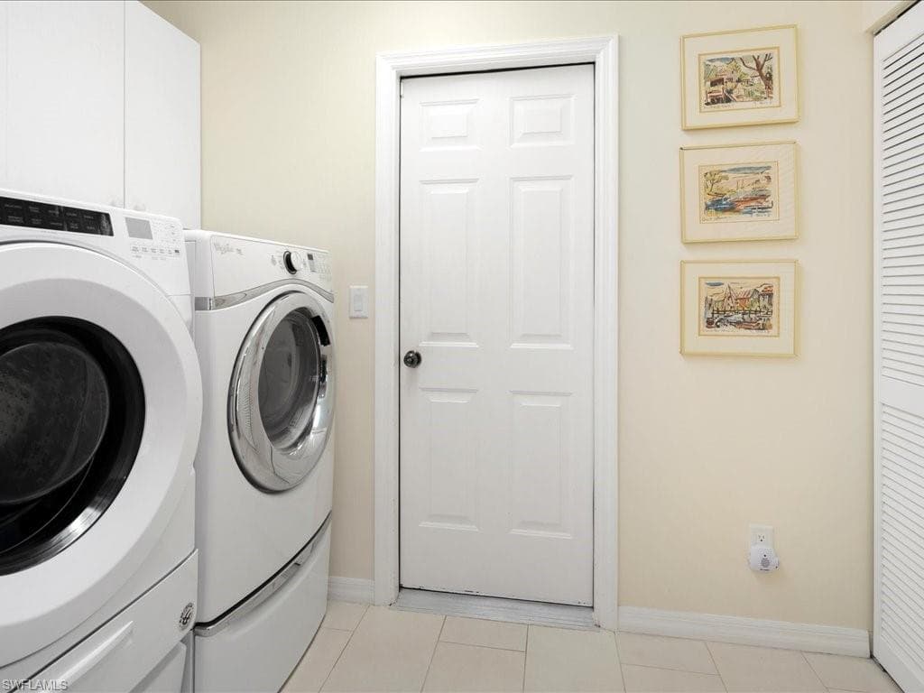 Clothes washing area featuring cabinets, washing machine and clothes dryer, and light tile patterned flooring