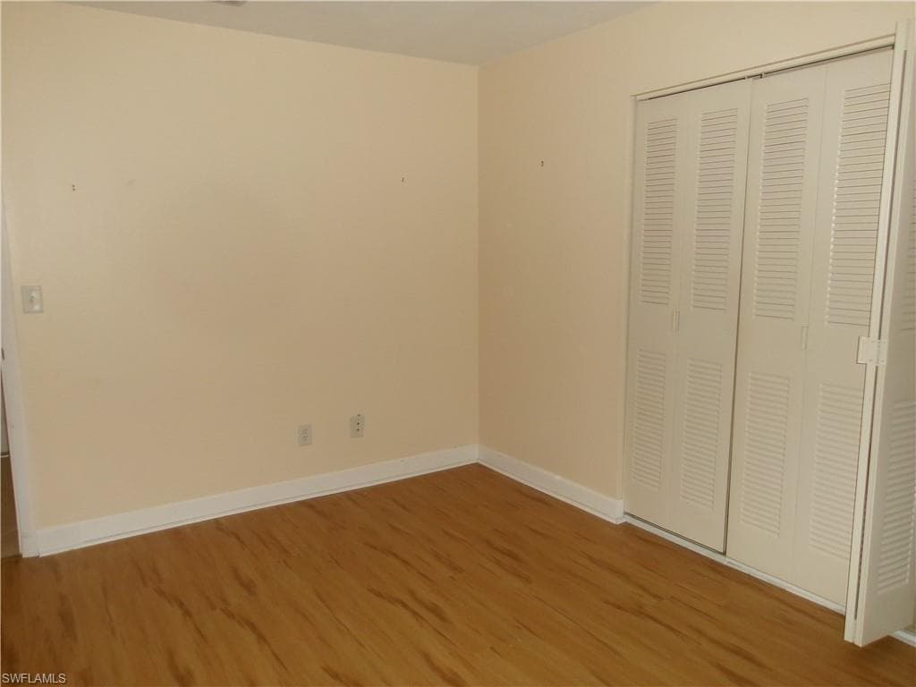 Unfurnished bedroom with a closet, wood finished floors, and baseboards
