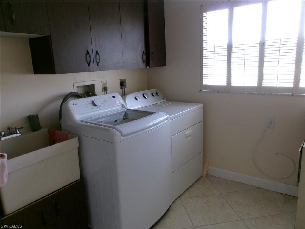Laundry area featuring cabinet space, light tile patterned floors, baseboards, washer and clothes dryer, and a sink