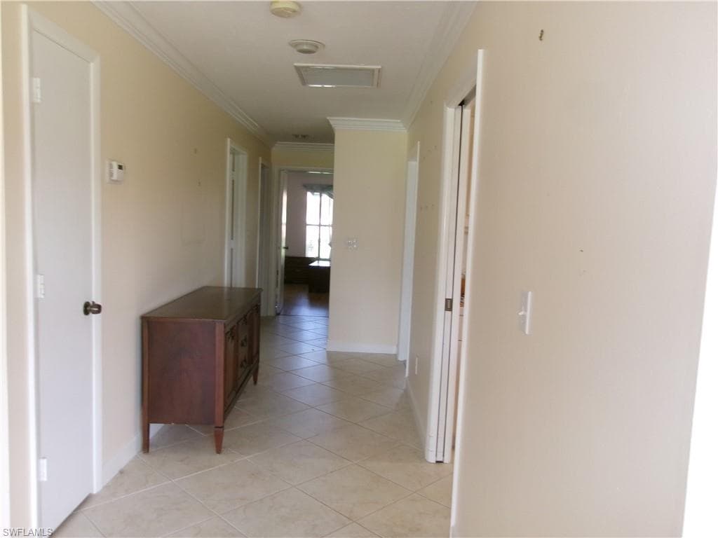 Hallway with light tile patterned floors, ornamental molding, and baseboards