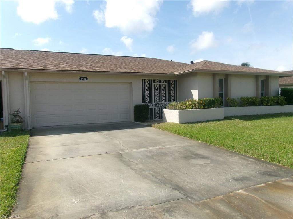 Ranch-style house with an attached garage, a front lawn, concrete driveway, and stucco siding