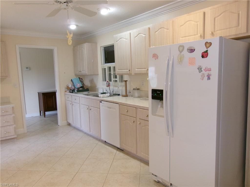 Kitchen featuring light tile patterned flooring, white appliances, a sink, light countertops, and ornamental molding