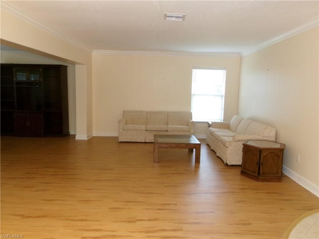 Unfurnished living room featuring ornamental molding, light wood-type flooring, visible vents, and baseboards
