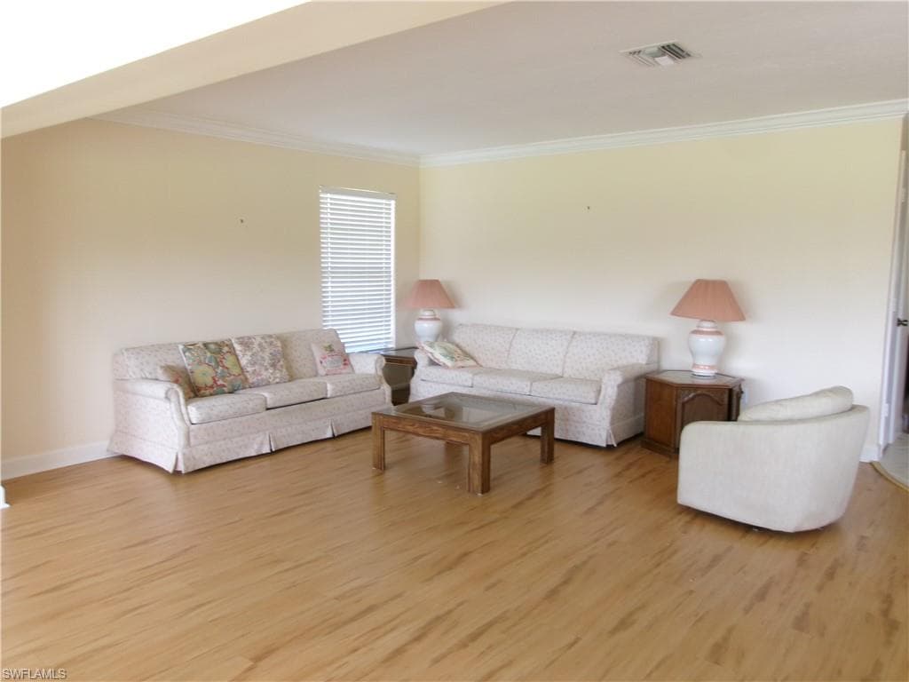 Living room featuring baseboards, light wood-type flooring, visible vents, and crown molding