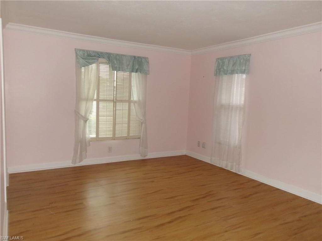 Empty room featuring baseboards, wood finished floors, and crown molding