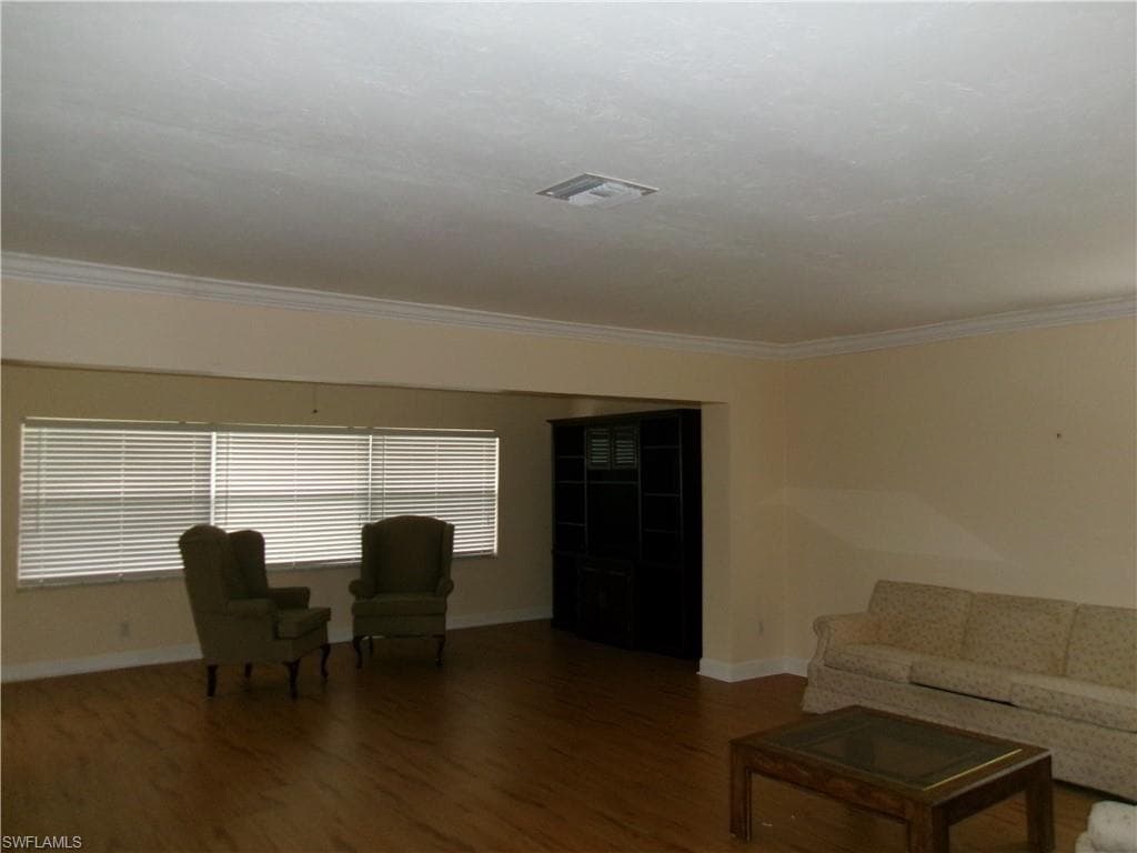 Living room with ornamental molding, dark wood-style flooring, visible vents, and baseboards