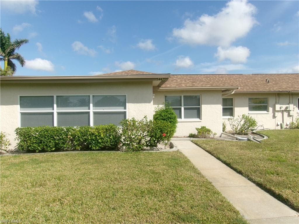View of front of house with a shingled roof, a front yard, and stucco siding
