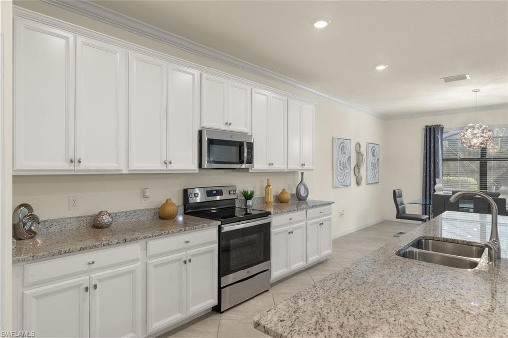 Kitchen with appliances with stainless steel finishes, sink, pendant lighting, white cabinets, and light stone countertops