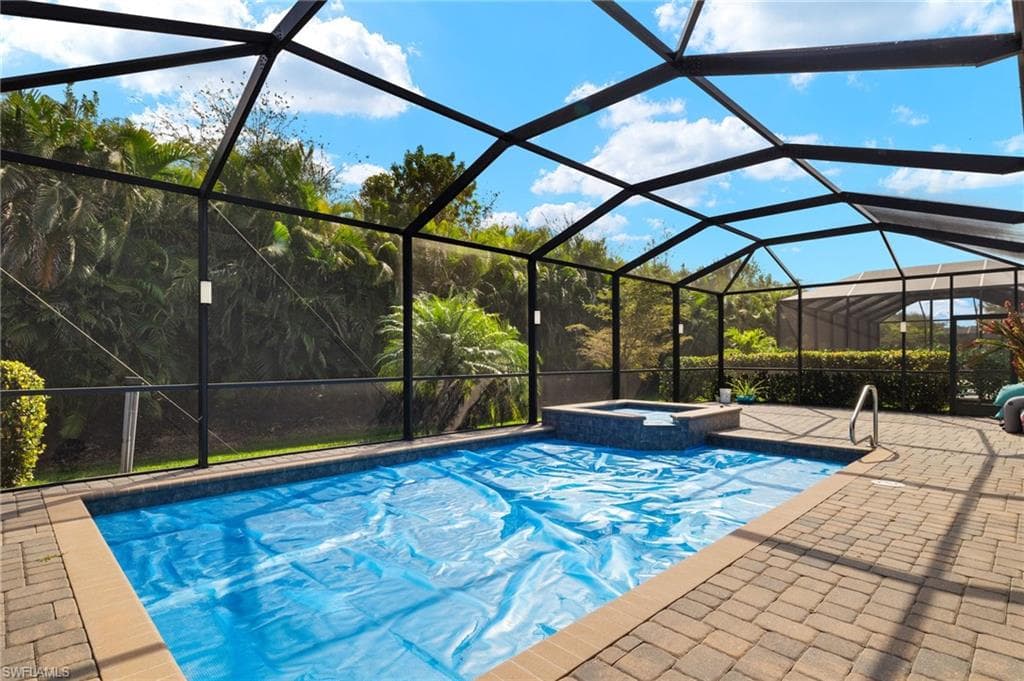 View of swimming pool with an in ground hot tub, glass enclosure, and a patio area