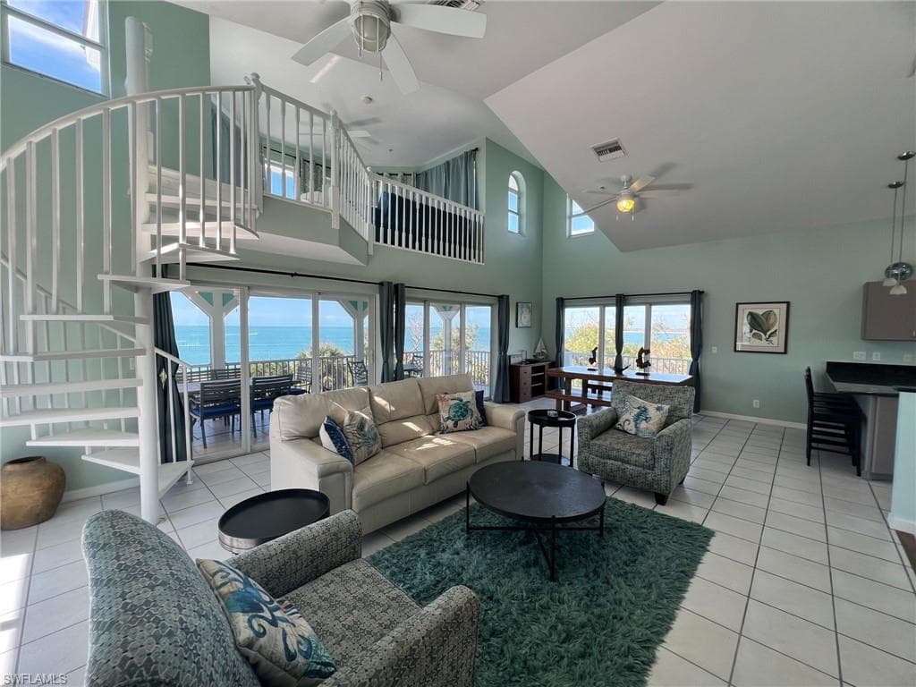 Living room featuring light tile patterned floors, visible vents, baseboards, ceiling fan, and a water view