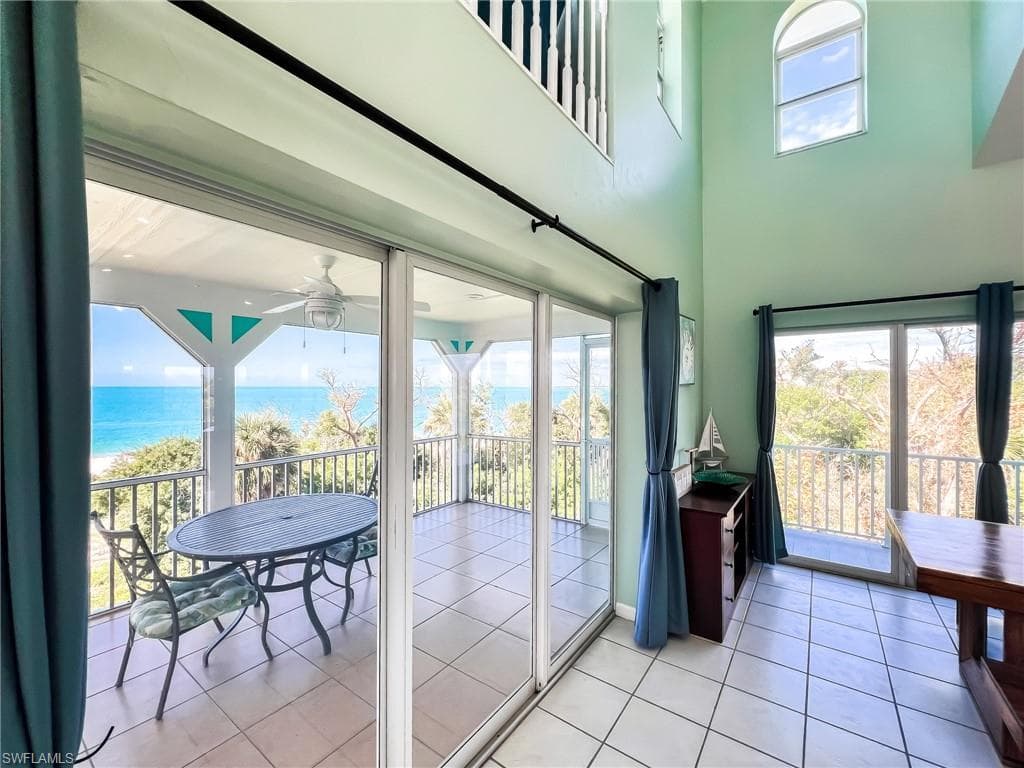 Doorway to outside featuring light tile patterned floors, ceiling fan, a water view, and a towering ceiling