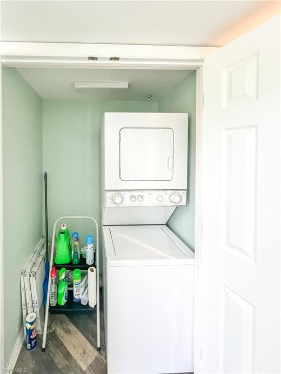 Washroom featuring laundry area, wood finished floors, stacked washer and clothes dryer, and baseboards