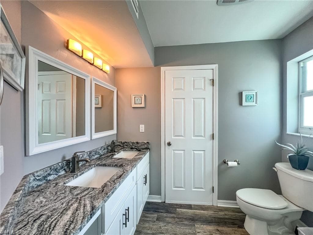 Bathroom with double vanity, a sink, toilet, and wood finished floors