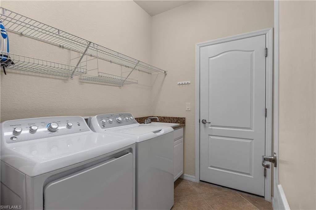 Laundry room leading out to garage, featuring tile patterned floors, a wash sink, storage space, and washer and dryer