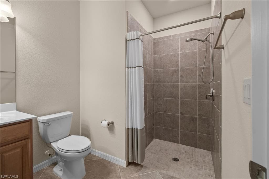 En-suite second bathroom featuring tile patterned flooring, toilet, vanity, baseboards, and a tile shower
