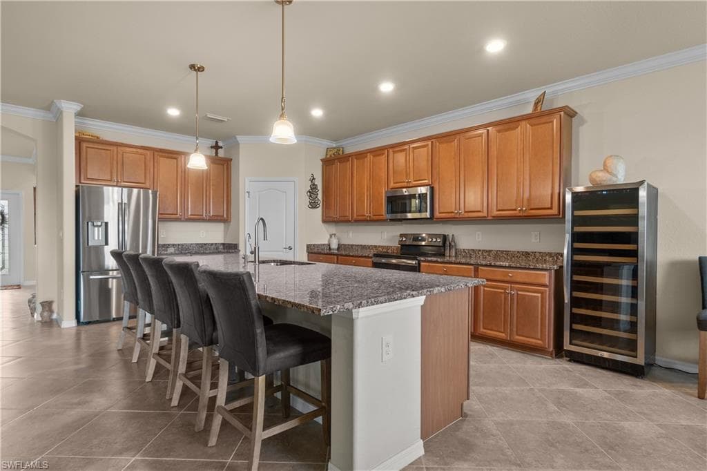 Kitchen featuring wine cooler, stainless steel appliances, a sink, brown cabinetry, and an island with sink