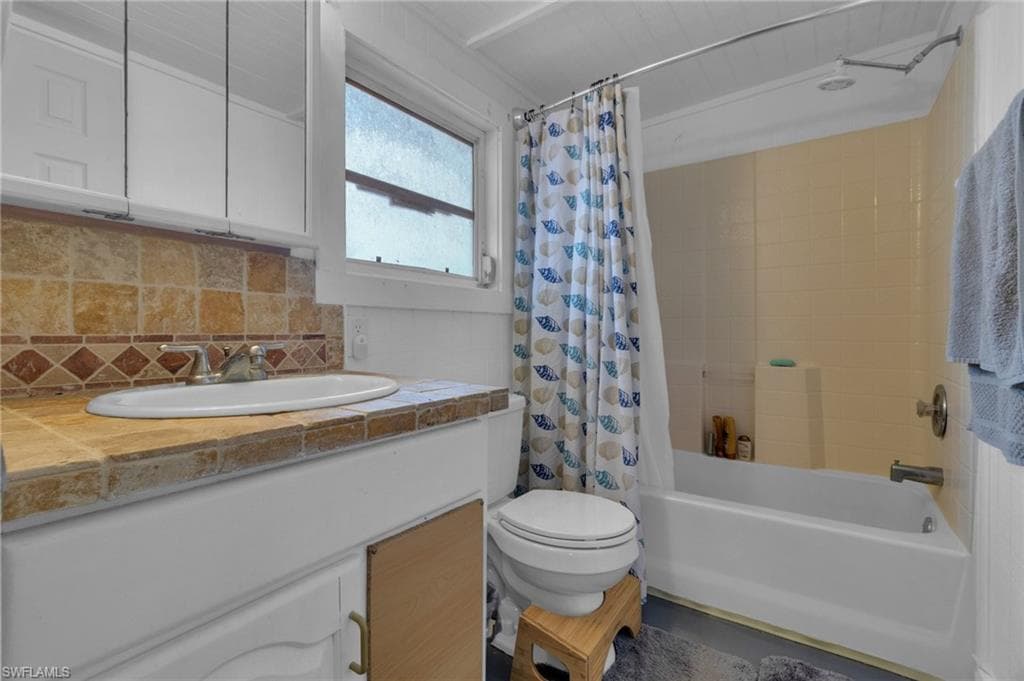 Bathroom featuring toilet, backsplash, shower / tub combo with curtain, and vanity