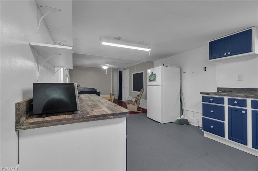 Kitchen with blue cabinetry, open shelves, butcher block counters, and freestanding refrigerator