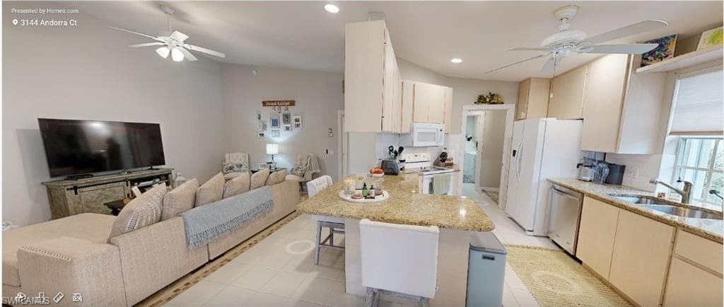 Kitchen with a ceiling fan, open floor plan, a peninsula, white appliances, and a kitchen breakfast bar