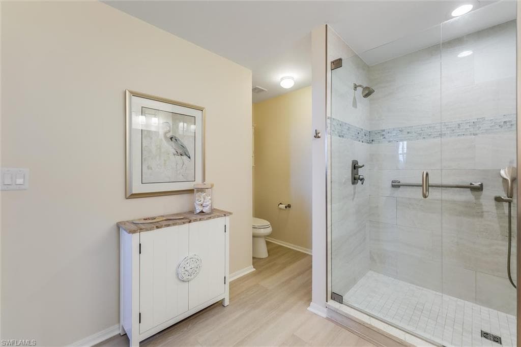 Bathroom with toilet, a shower stall, baseboards, and wood finished floors