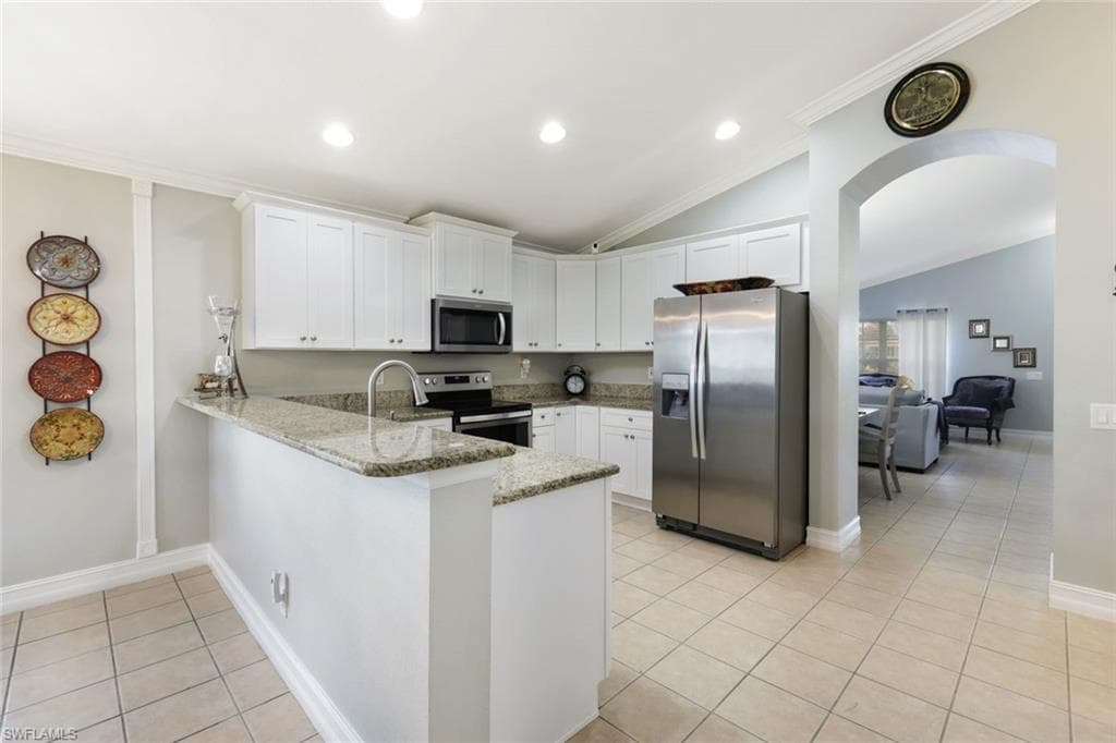 Kitchen with light tile patterned floors, arched walkways, white cabinets, a peninsula, and stainless steel appliances