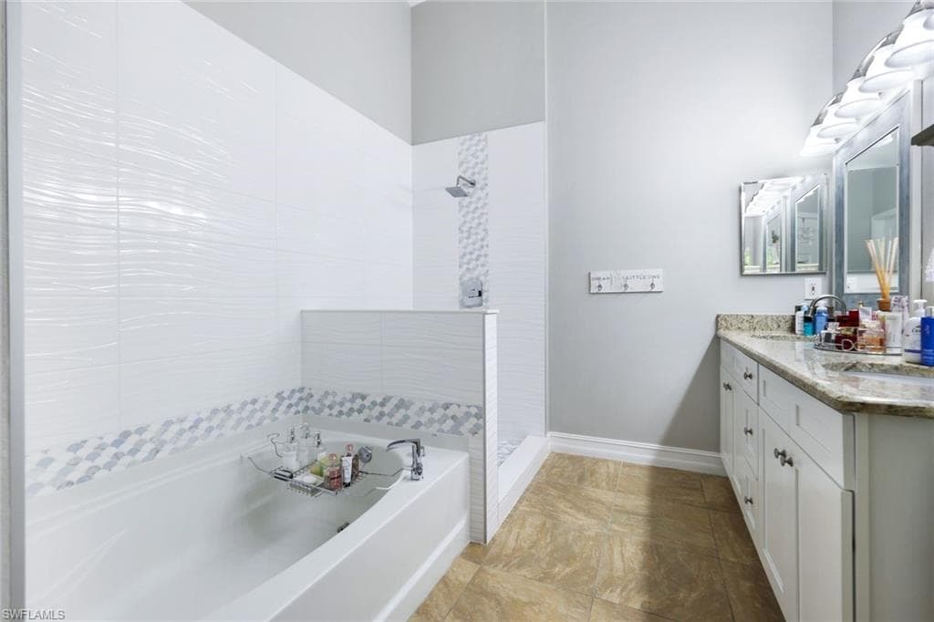 Full bathroom with double vanity, a sink, a tile shower, baseboards, and a bath