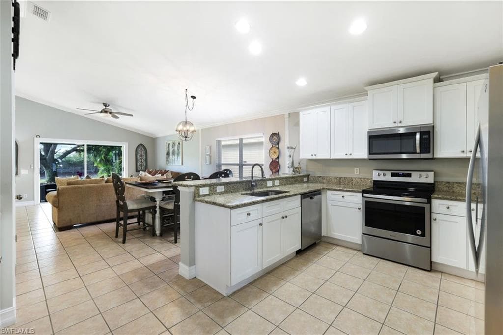 Kitchen with light tile patterned floors, appliances with stainless steel finishes, open floor plan, a peninsula, and a sink