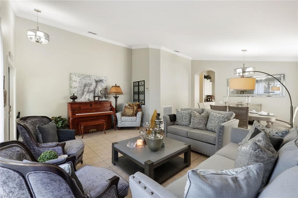 Living room with light tile patterned floors, visible vents, arched walkways, and crown molding