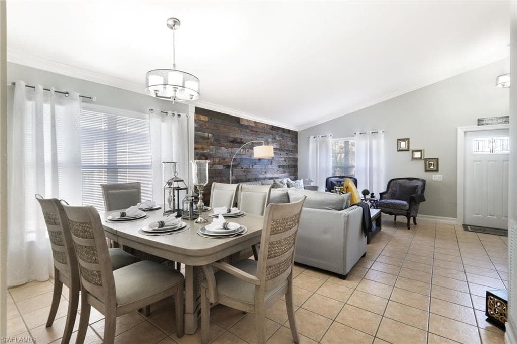 Dining area with light tile patterned floors, an accent wall, vaulted ceiling, and crown molding