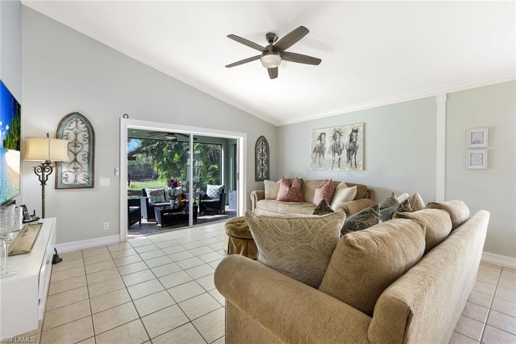 Living room with light tile patterned floors, lofted ceiling, a ceiling fan, baseboards, and crown molding