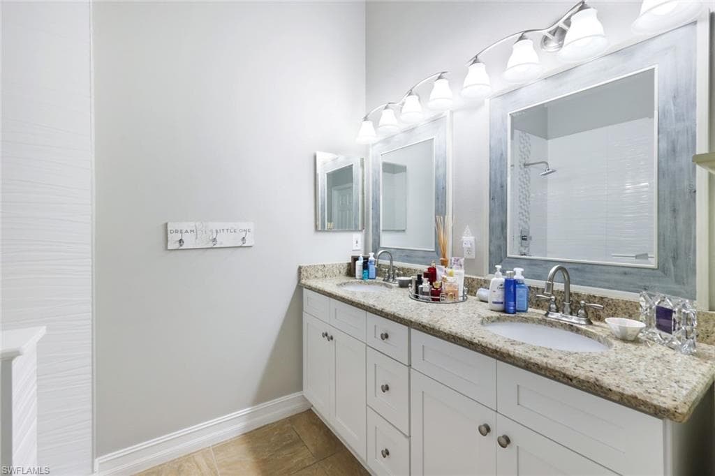 Full bathroom featuring double vanity, tiled shower, a sink, and baseboards