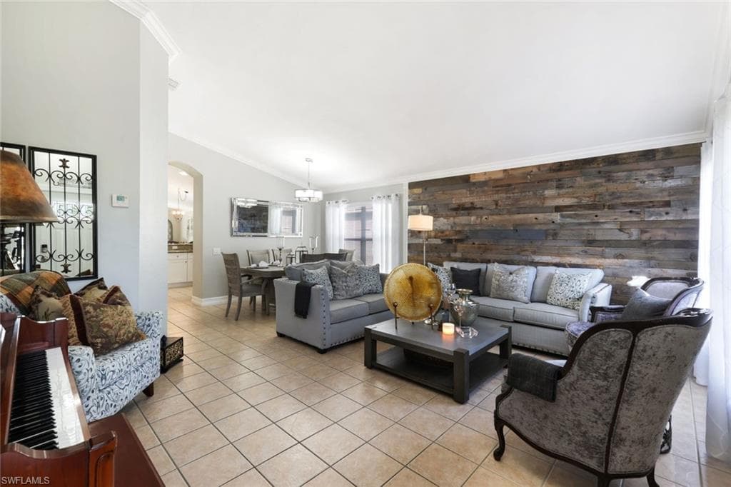 Living room with light tile patterned floors, arched walkways, an accent wall, vaulted ceiling, and crown molding