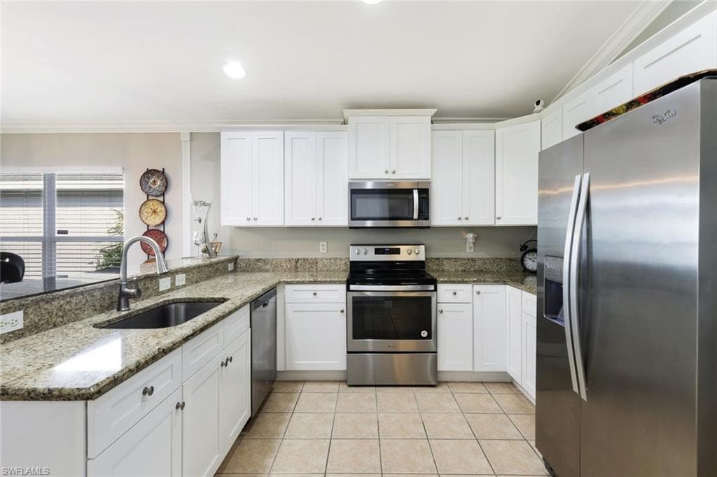 Kitchen with appliances with stainless steel finishes, white cabinets, a sink, and light tile patterned flooring