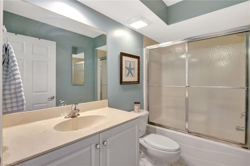 Full bath with shower / bath combination with glass door, vanity, and toilet
