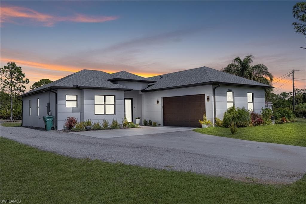 View of front of house featuring a yard, stucco siding, a shingled roof, concrete driveway, and a garage