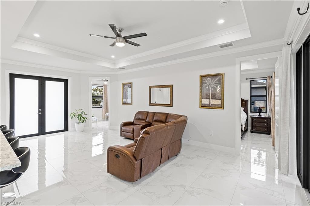 Living room with a tray ceiling, french doors, visible vents, and marble finish floor