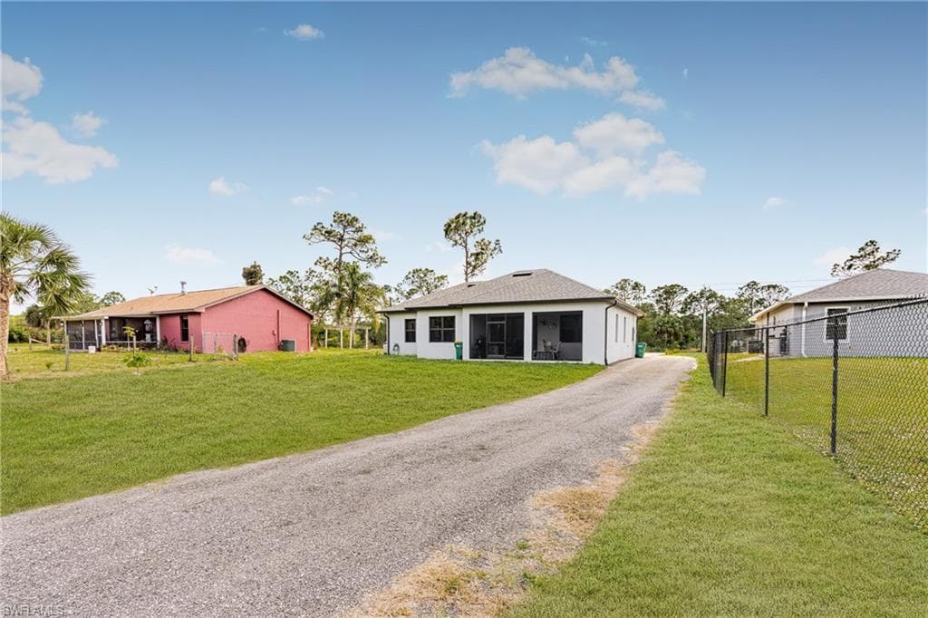 View of front of property with gravel driveway, a sunroom, fence, and a front lawn