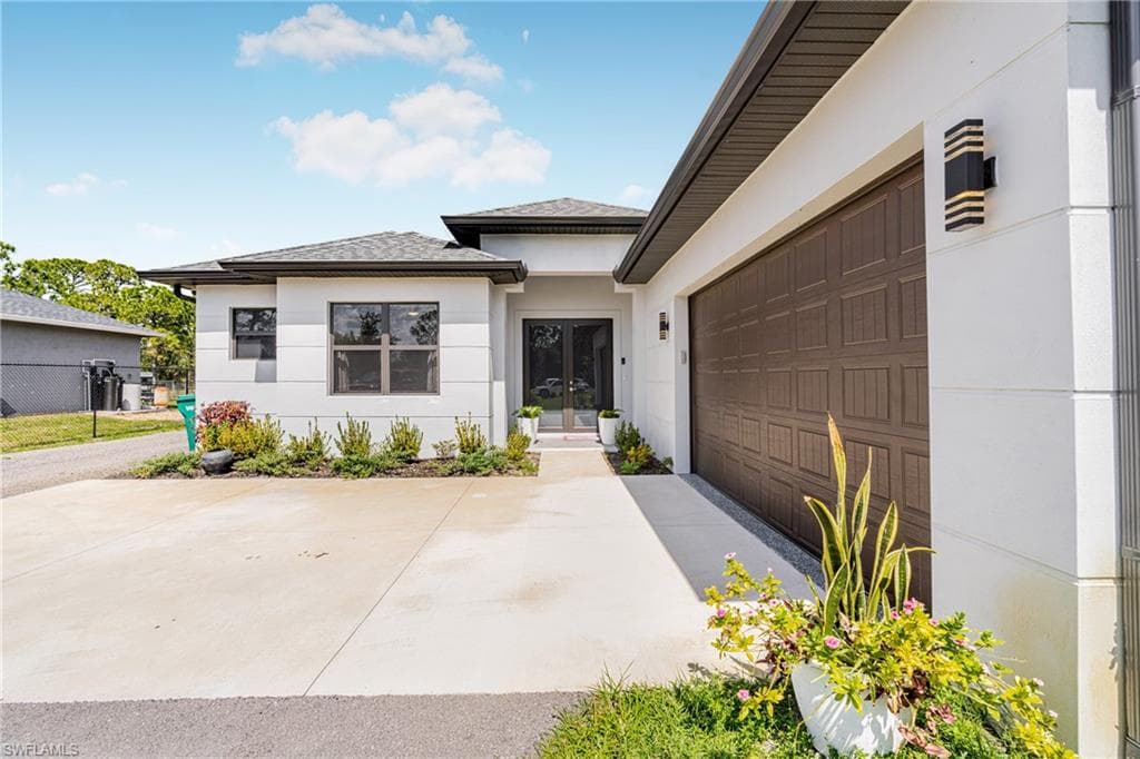 Entrance to property featuring a garage, concrete driveway, french doors, and stucco siding