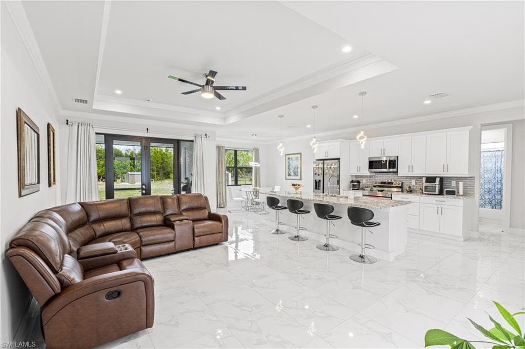 Living area with a tray ceiling, marble finish floor, crown molding, and french doors