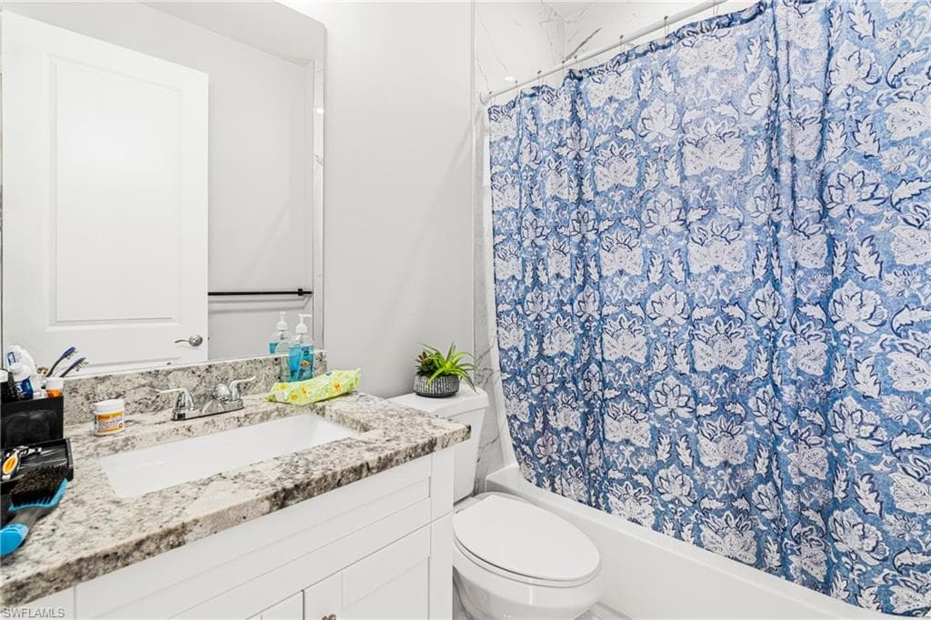 Full bathroom with shower / bath combo with shower curtain, vanity, and toilet