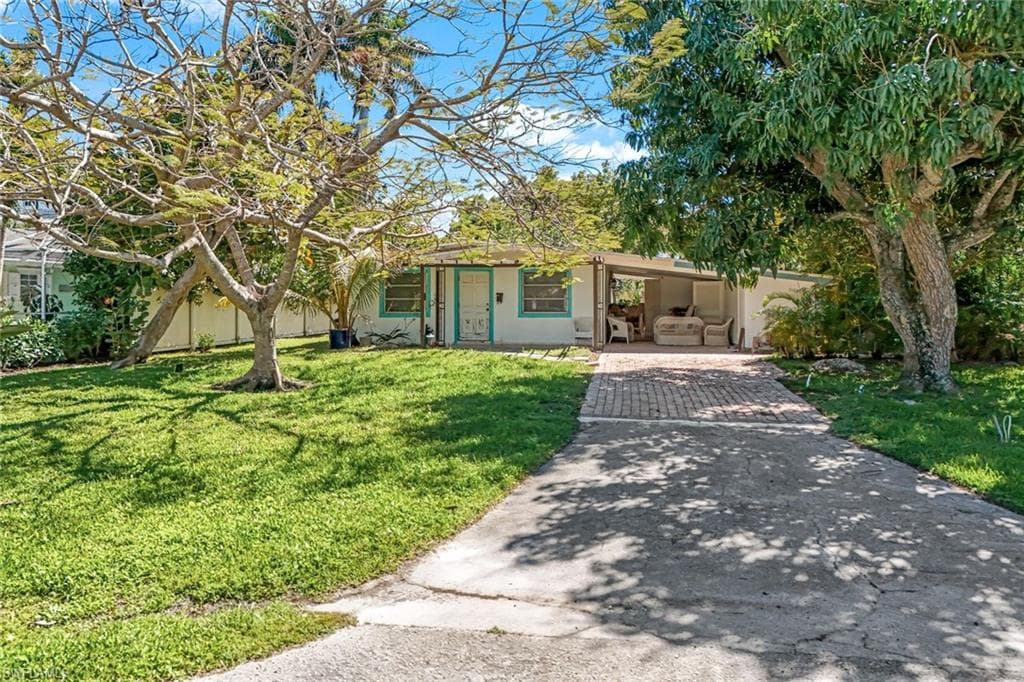 View of front of house featuring an attached carport, a front yard, driveway, and stucco siding