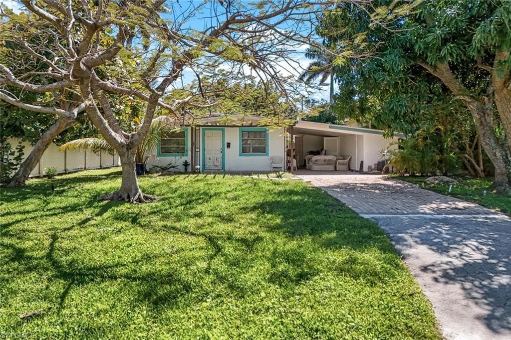 View of front of home with an attached carport, fence, a front yard, stucco siding, and decorative driveway