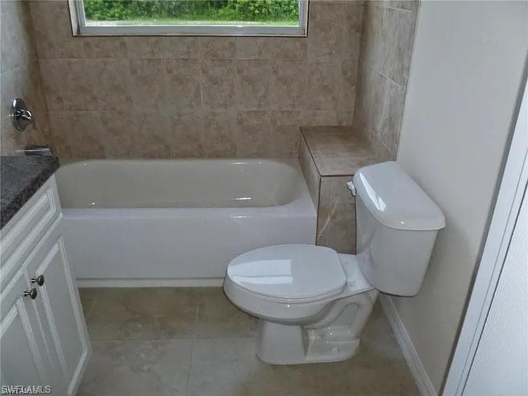 Bathroom featuring tile patterned flooring, a healthy amount of sunlight, toilet, and a tub to relax in